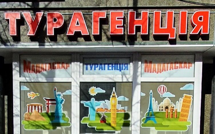 Вхід до турагенції: червона вивіска «Турагенція» над вітриною з написом «Мадагаскар» на Соборній, 31