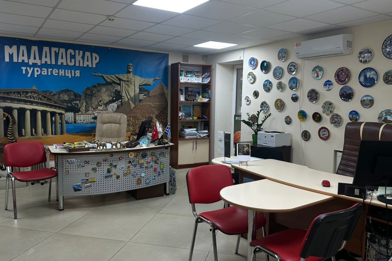 Офіс «Мадагаскару» на Соборній: банер «Мадагаскар турагенція», стіна із сувенірними тарілками й масками з подорожей, стіл менеджерки, обліплений магнітами